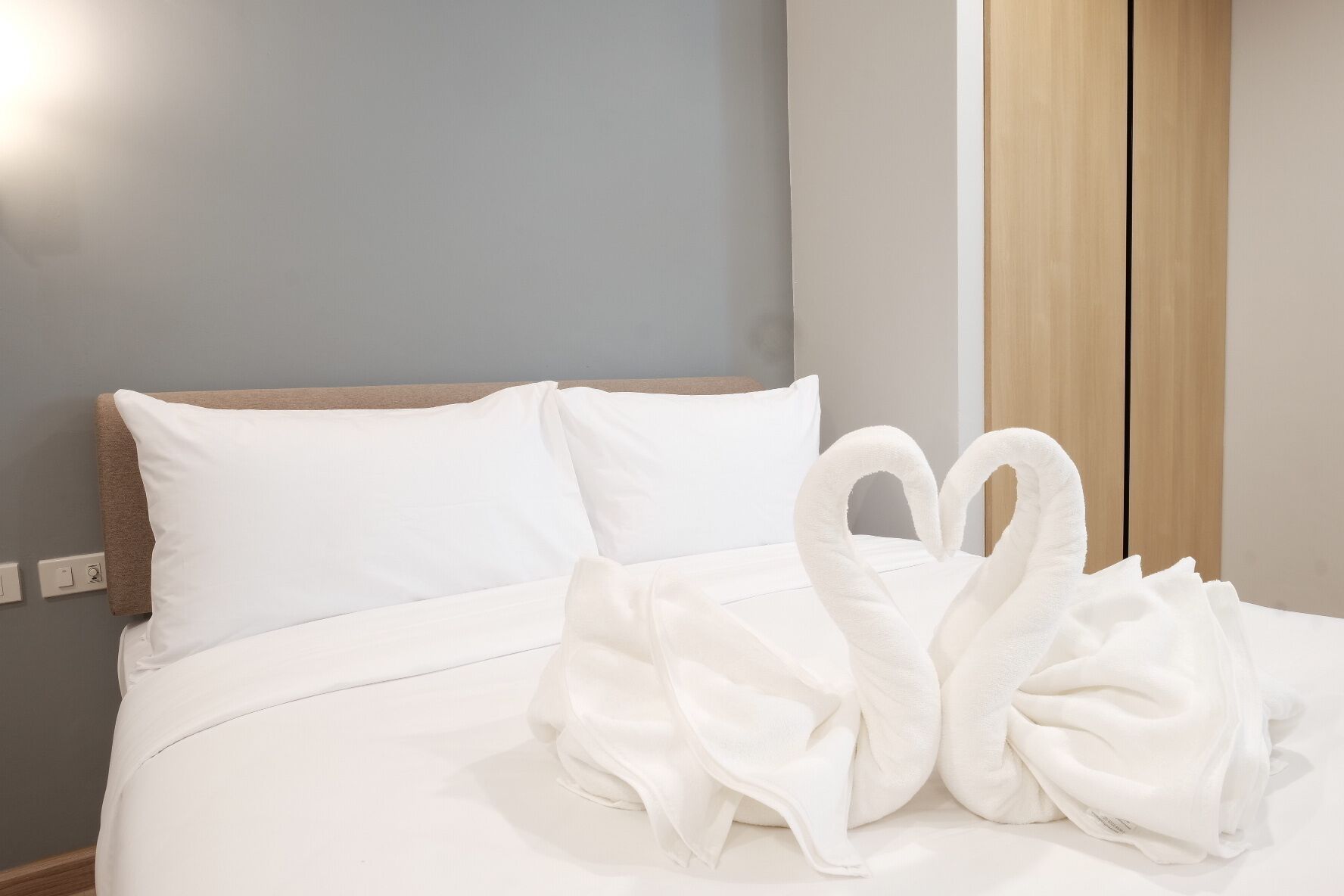 Un lit bien fait, avec du linge de lit blanc et deux serviettes disposées en forme de cygnes.