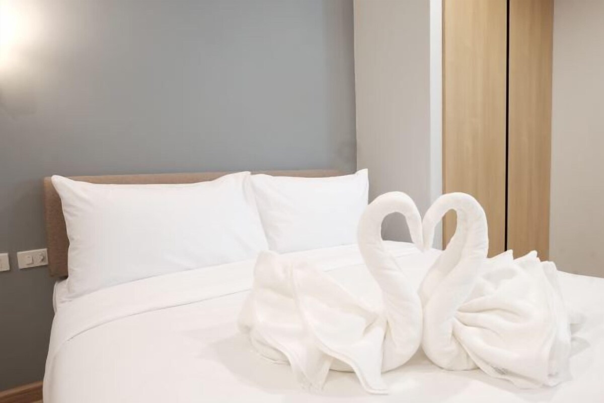 Una cama bien hecha con sábanas blancas y dos toallas blancas dispuestas en forma de corazón.