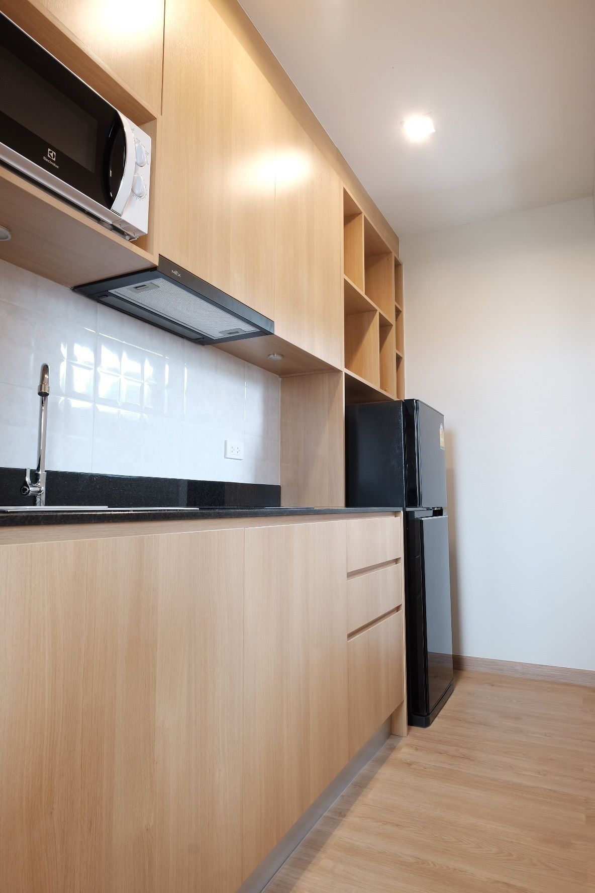 Una cocina moderna con armarios de madera, un refrigerador negro y un microondas.