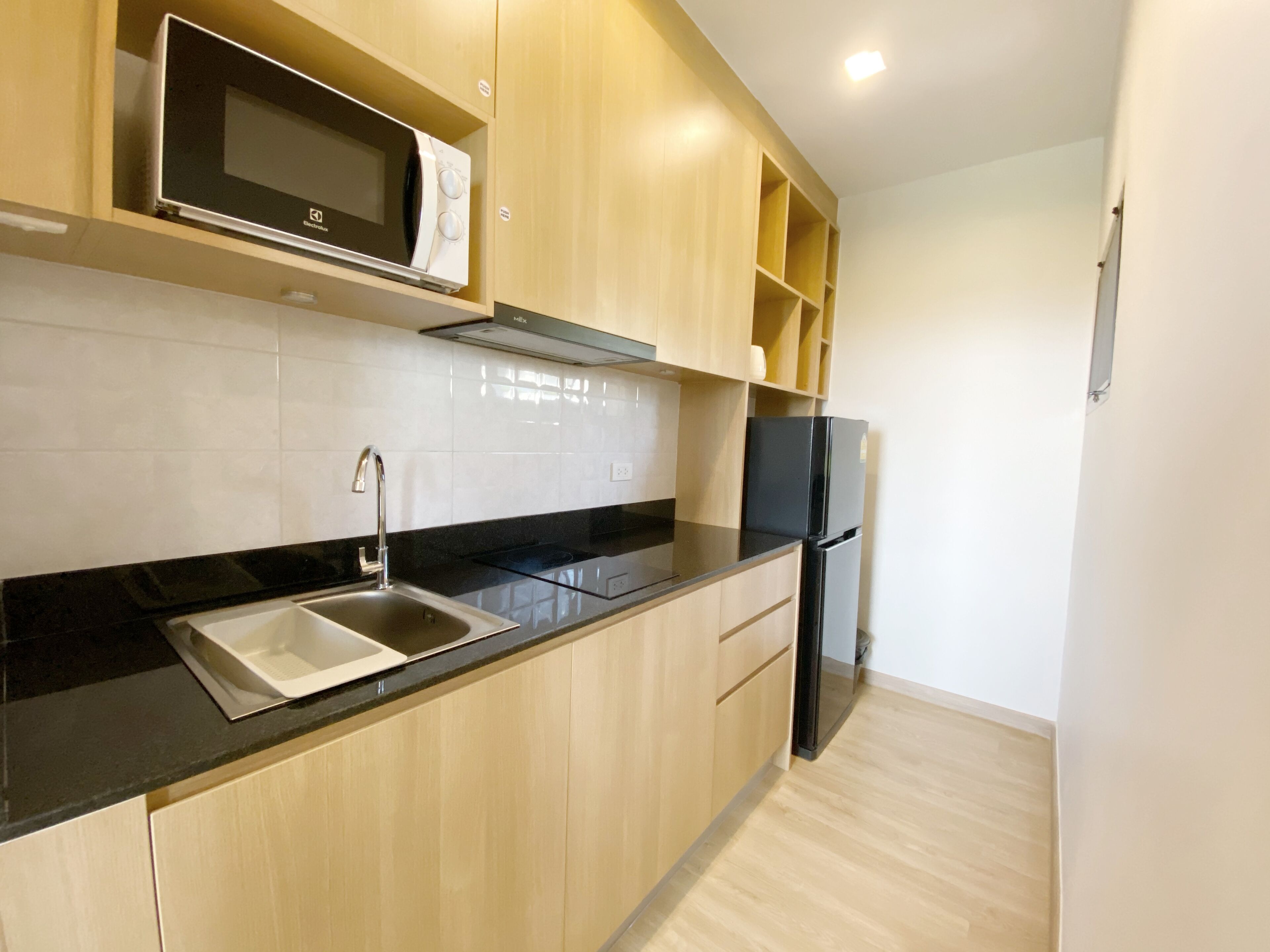 Een moderne keuken met een zwart aanrecht, een roestvrijstalen spoelbak, houten kastjes, een zwarte koelkast en een magnetron op het bovenste plankje.