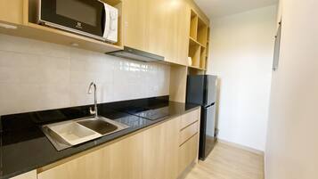 A modern kitchen with a black countertop, stainless steel sink, wooden cabinets, a black refrigerator, and a microwave on the upper shelf.
