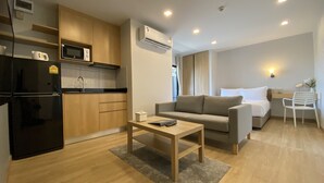 Eine moderne Wohnung mit Küche, Wohnbereich und Schlafzimmer. Sie umfasst einen Kühlschrank, eine Mikrowelle, ein Spülbecken, ein Sofa und ein Bett.