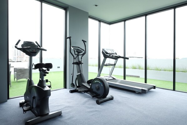 A modern gym with cardio equipment and large windows overlooking a green outdoor area.