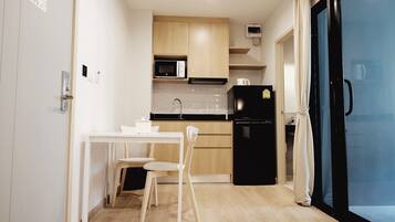 A compact kitchen with a dining table and chairs, a microwave, a refrigerator, and a small window.