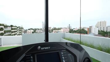 Equipamento de ginástica com visor digital e painel de controle, com vista para um horizonte urbano com edifícios e áreas verdes.