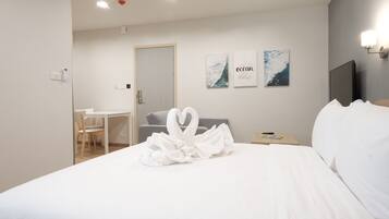 A hotel room with a bed, a desk, a chair, and a TV. There are wall art pieces and a heart-shaped towel on the bed.