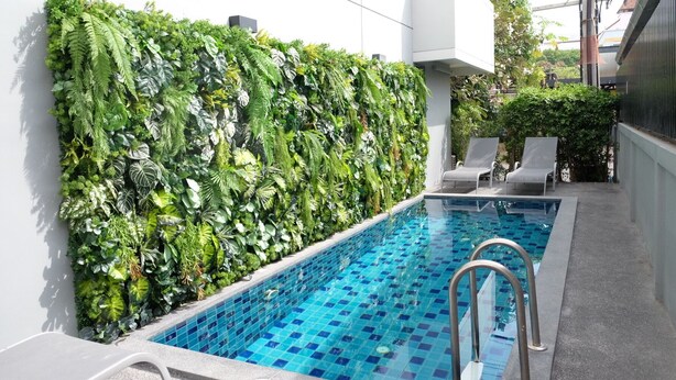 Ein Pool mit Fliesenrand, umgeben von Liegestühlen und einer vertikalen Grünwand.