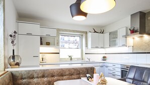A modern kitchen with white cabinetry, a large window, and a dining area with a tufted bench. - Apartment Naturnah (Kauns)