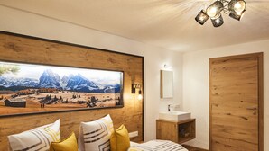 A bedroom with a large bed, wooden headboard, a painting of mountains, a wooden wardrobe, and a bedside table with a mirror. - Apartment Naturnah (Kauns)