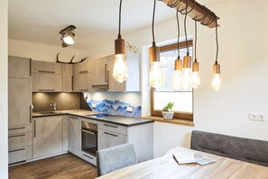 A modern kitchen with wooden cabinets, a built-in stove, and a dining area with a table and bench.