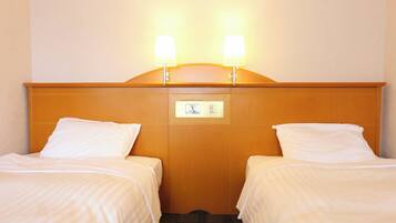 Ett hotellrum med två separata sängar, en sänggavel i trä och två sänglampor.