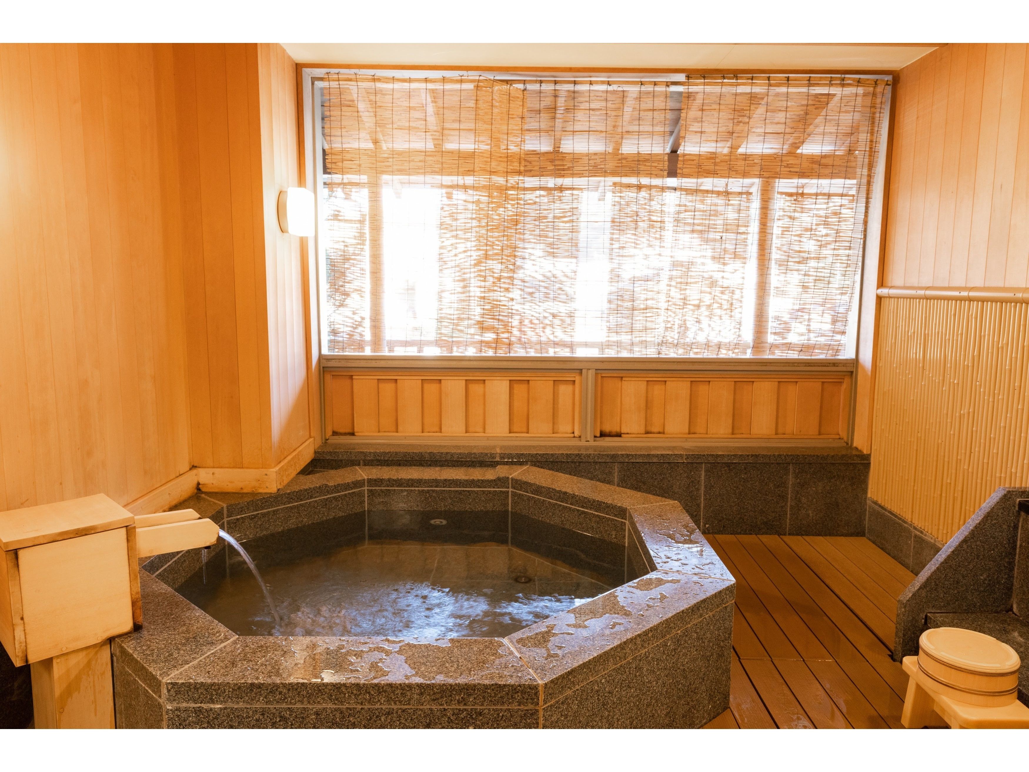 A hot spring bath with a wooden interior, a stone basin, and a window with bamboo blinds.