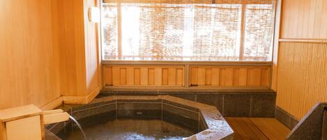 A hot spring bath with a wooden interior, a stone basin, and a window with bamboo blinds.