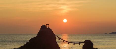 Um pôr do sol sobre um mar calmo, com duas formações rochosas, uma delas com uma pequena construção no topo.