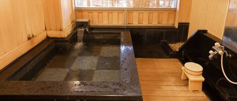 A traditional Japanese onsen with a wooden interior, a stone hot spring, and a wooden toilet.