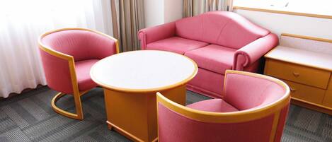 A hotel room with a pink sofa, two matching armchairs, a small round table, and a wooden nightstand.