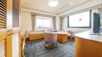 A hotel room with a large window, a television, a desk, and two chairs.