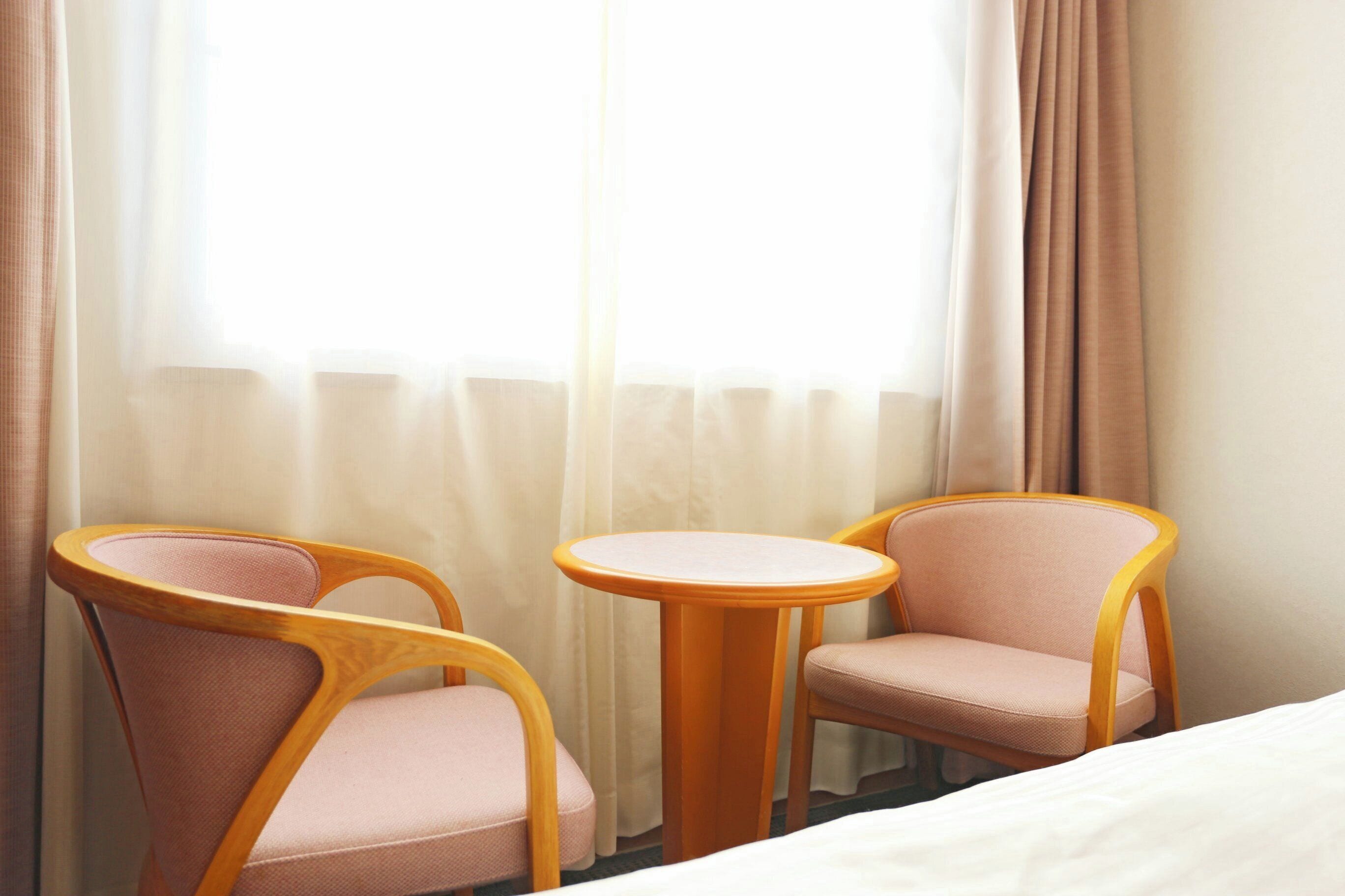 Ein Hotelzimmer mit einem Bett, zwei Holzstühlen mit rosafarbenen Kissen und einem kleinen runden Tisch.