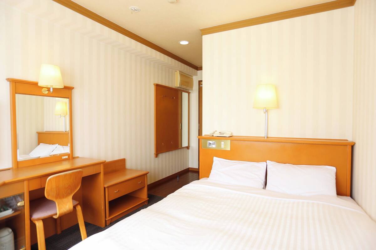 Una habitación de hotel con cama, escritorio, silla y espejo.