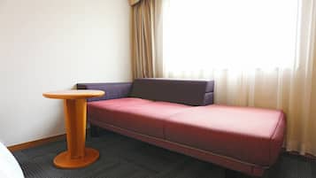 A room with a single bed, a small round table, a sofa, and a window with curtains.