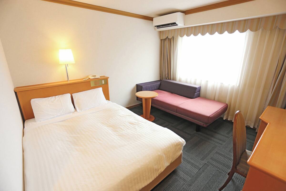 Una habitación de hotel con cama, sofá, una mesita redonda y un escritorio.