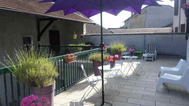 Eine Terrasse mit einem violetten Sonnenschirm, Topfpflanzen und Sitzgelegenheiten.