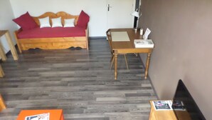 Ein Zimmer mit einem Holzsofa, einem Esstisch, einem orangefarbenen Tisch und einem Holzkasten mit einer Computermaus.