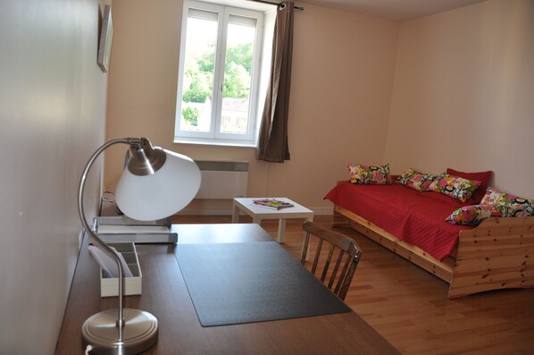 Un dormitorio con una cama de madera, un escritorio con lámpara, una mesita y una ventana con cortinas.