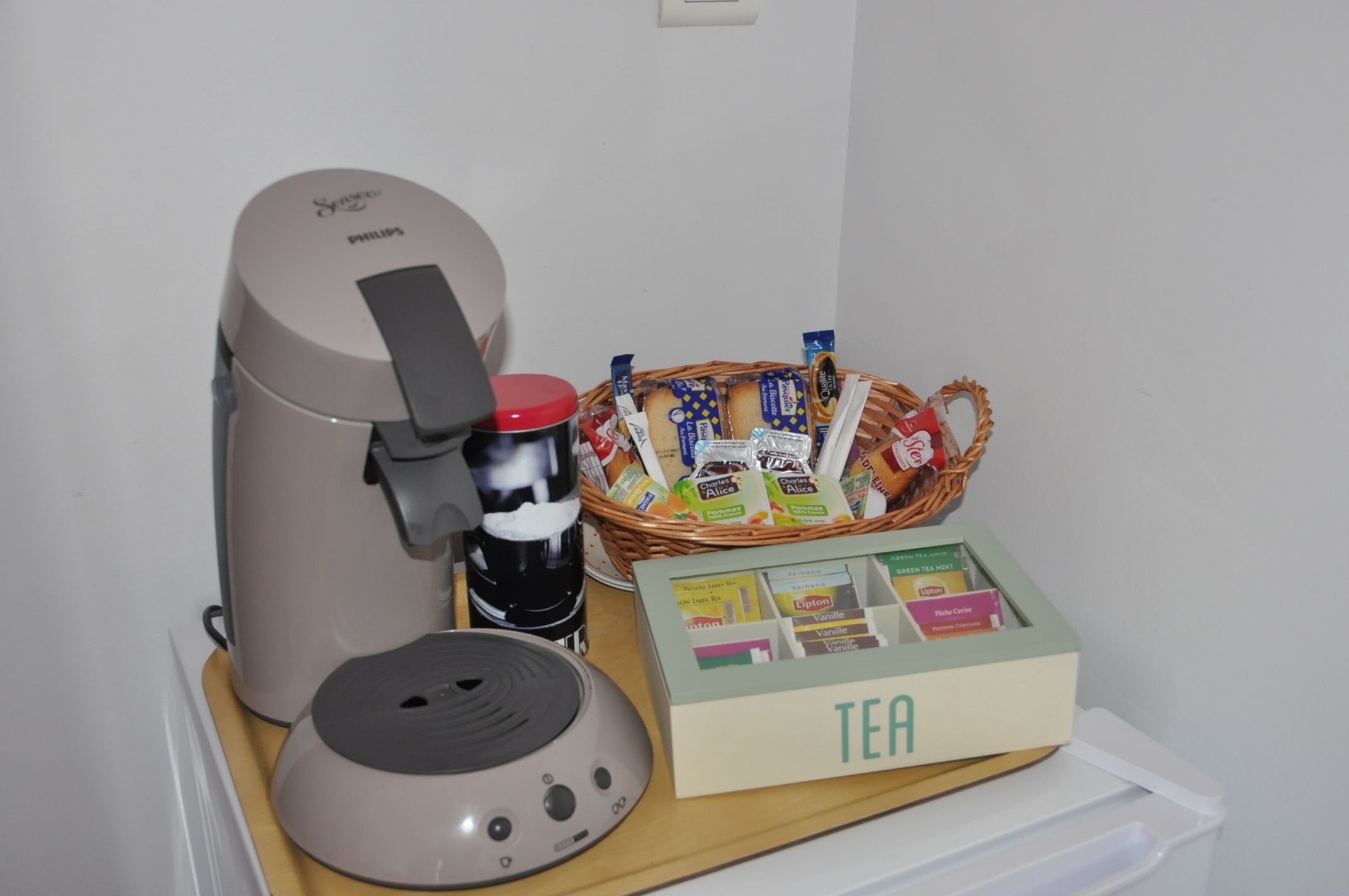 A coffee maker, a basket of tea bags, and a box of Lipton tea on a table.