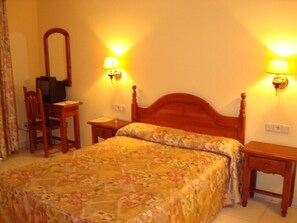 A bedroom with a wooden bed, two bedside tables, a chair, a mirror, and two wall-mounted lamps.