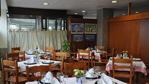 A restaurant with tables set for dining, wooden chairs, and a view of the outside through large windows. - Boncompte (Ponts)