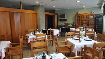 Un restaurante con mesas y sillas de madera, manteles blancos y un televisor montado en la pared.