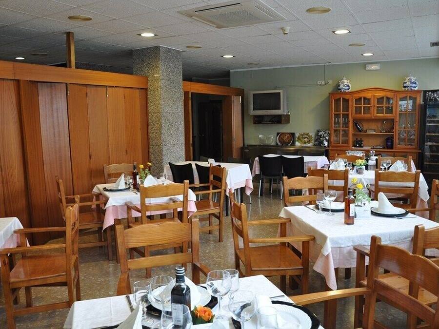 Un restaurante con mesas y sillas de madera, manteles blancos y un televisor montado en la pared.