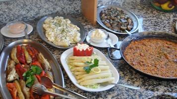 Variedad de platos sobre una encimera de granito, incluyendo mariscos, verduras y una fuente grande de lo que parece ser un plato al horno.