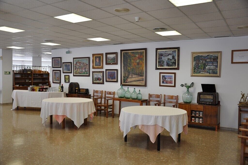 Uma área de refeições com mesas e cadeiras, obras de arte emolduradas nas paredes e uma estante com garrafas e um rádio.