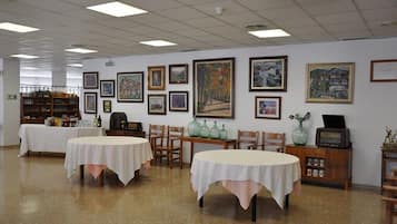 Uma área de refeições com mesas e cadeiras, obras de arte emolduradas nas paredes e uma estante com garrafas e um rádio.