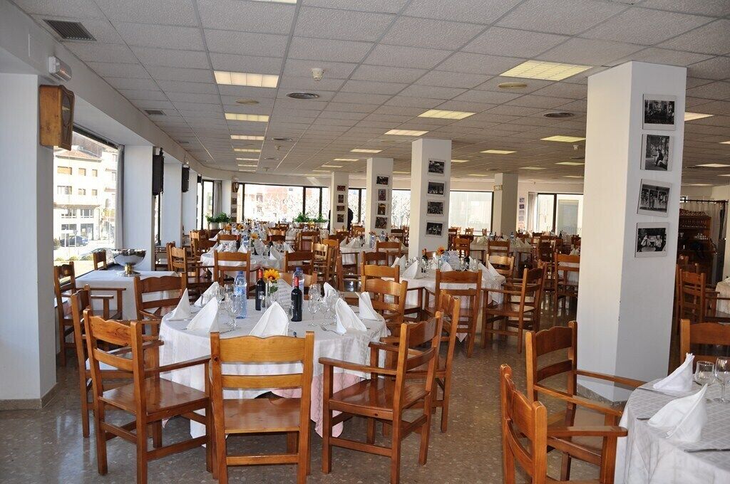 Un comedor amplio con varias mesas y sillas, ventanas grandes que ofrecen luz natural, y una distribución limpia y ordenada.