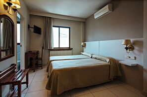A hotel room with two beds, a desk, a chair, a TV mounted on the wall, and a window with curtains.