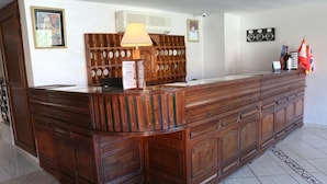 A reception desk with a wooden finish, a lamp, and a wall-mounted clock. - Hotel Saint-Antoine (Tafraout)