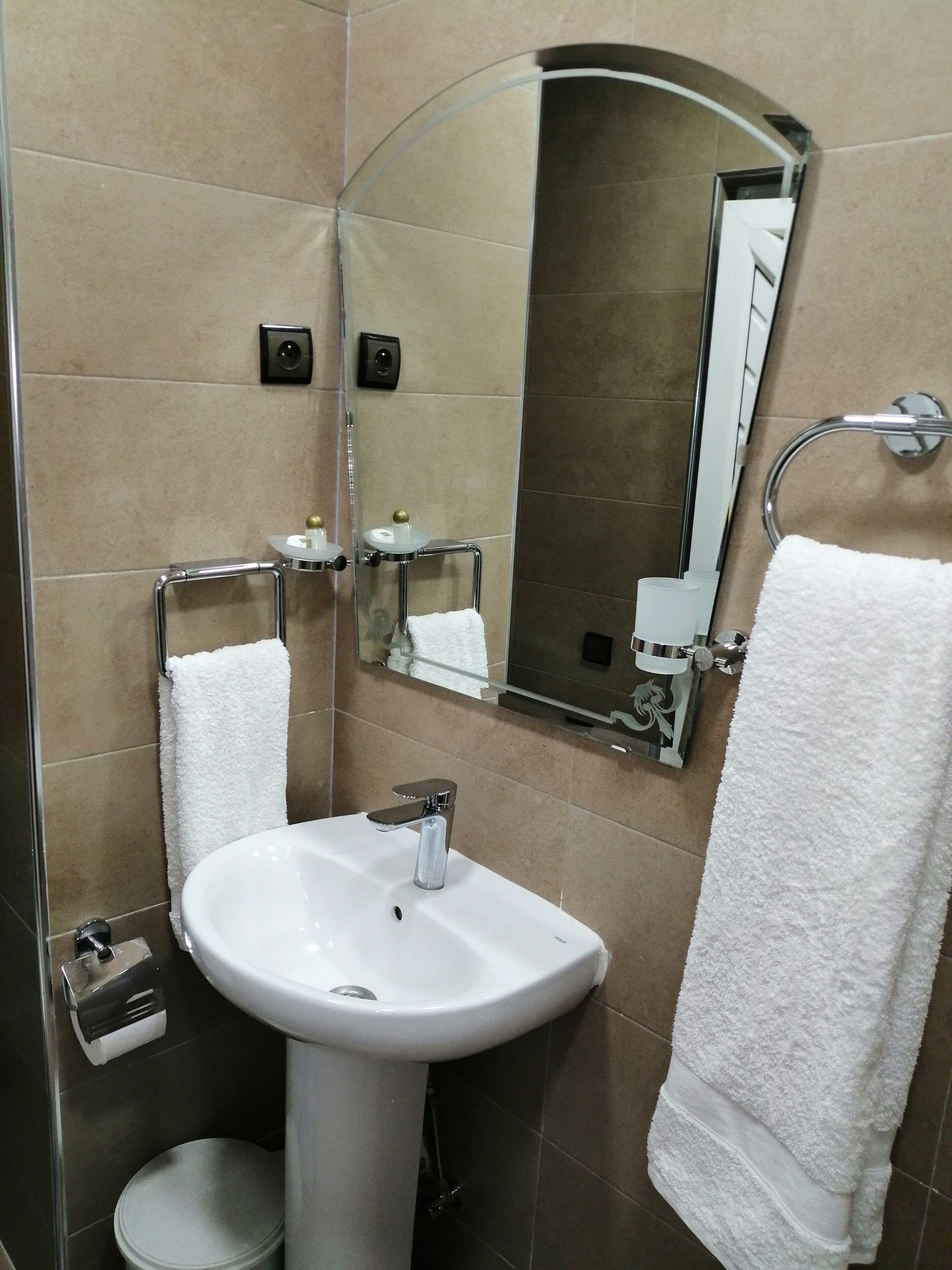 Un baño con un lavamanos blanco, un espejo y dos toallas colgadas en barras para toallas.