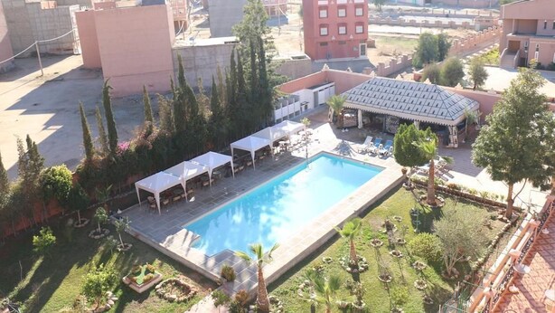 An aerial view of a hotel with a swimming pool surrounded by outdoor seating, greenery, and a mountainous backdrop. - Hotel Saint-Antoine (Tafraout)