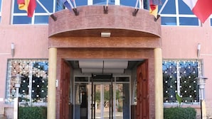 A building entrance with multiple flags, a green carpet, and a brick facade. - Hotel Saint-Antoine (Tafraout)