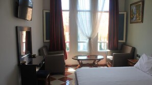 A hotel room with a bed, two armchairs, a small table, a TV mounted on the wall, and large windows with curtains. - Hotel Saint-Antoine (Tafraout)