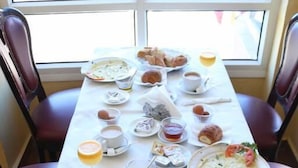 A breakfast table set with various dishes, including croissants, bread, and a bowl of soup, in a room with a large window. - Hotel Saint-Antoine (Tafraout)