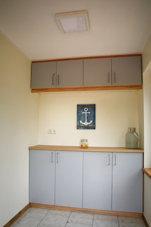 A kitchen with light grey cabinets, a wooden countertop, a small island with a jar of candies, and a blue anchor decoration on the wall. - Ferienwohnungen Möwe (Lembruch)