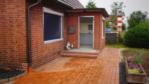 A brick house with a tiled patio, a small porch, and a garden with plants. - Ferienwohnungen Möwe (Lembruch)