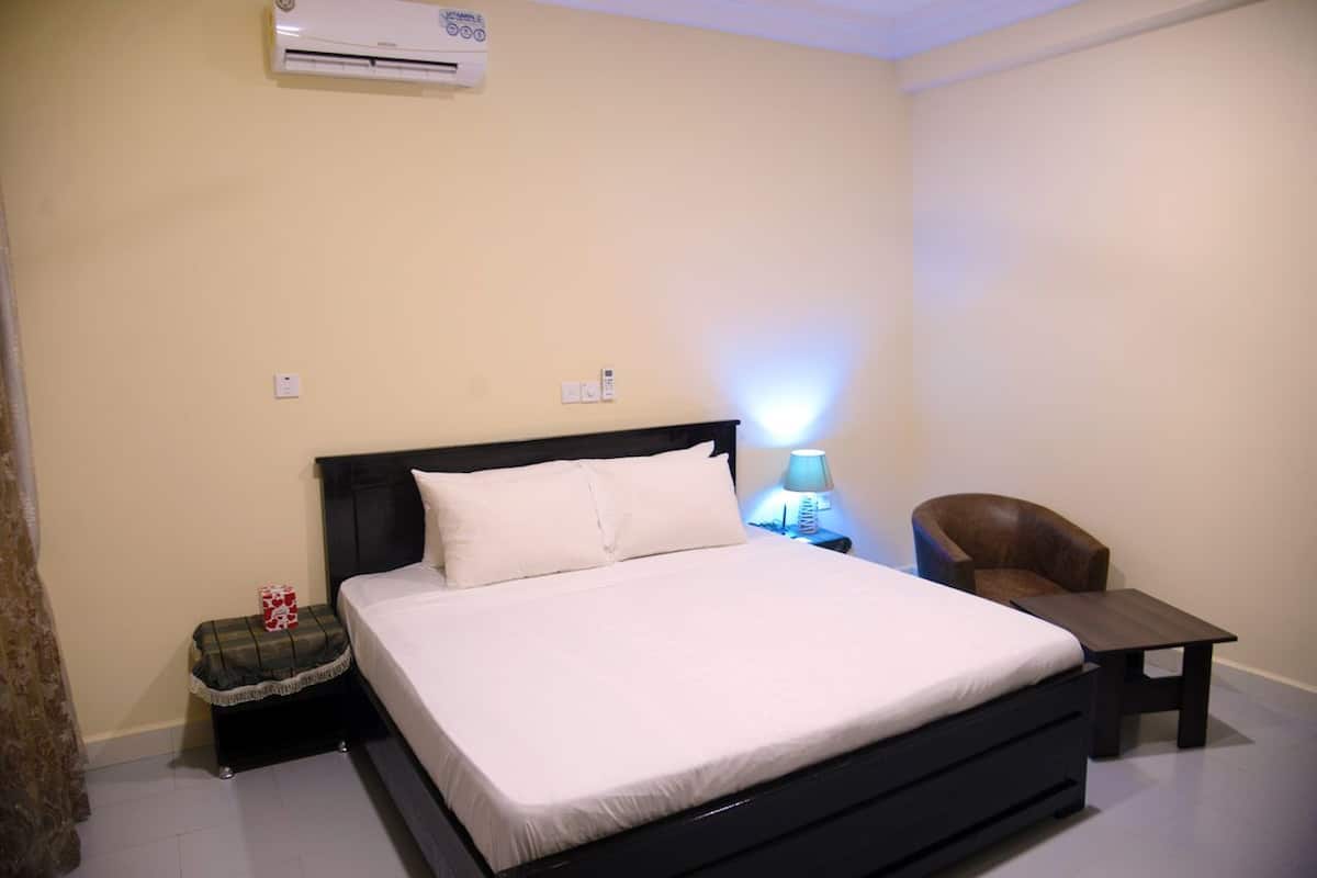 Une chambre à coucher comprenant un lit, une table de chevet, une lampe, une chaise et un climatiseur.