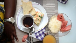 Ein Frühstücksteller mit Toast, Rührei, einer Tasse Kaffee, einem Glas Orangensaft und einer Schale Obst.