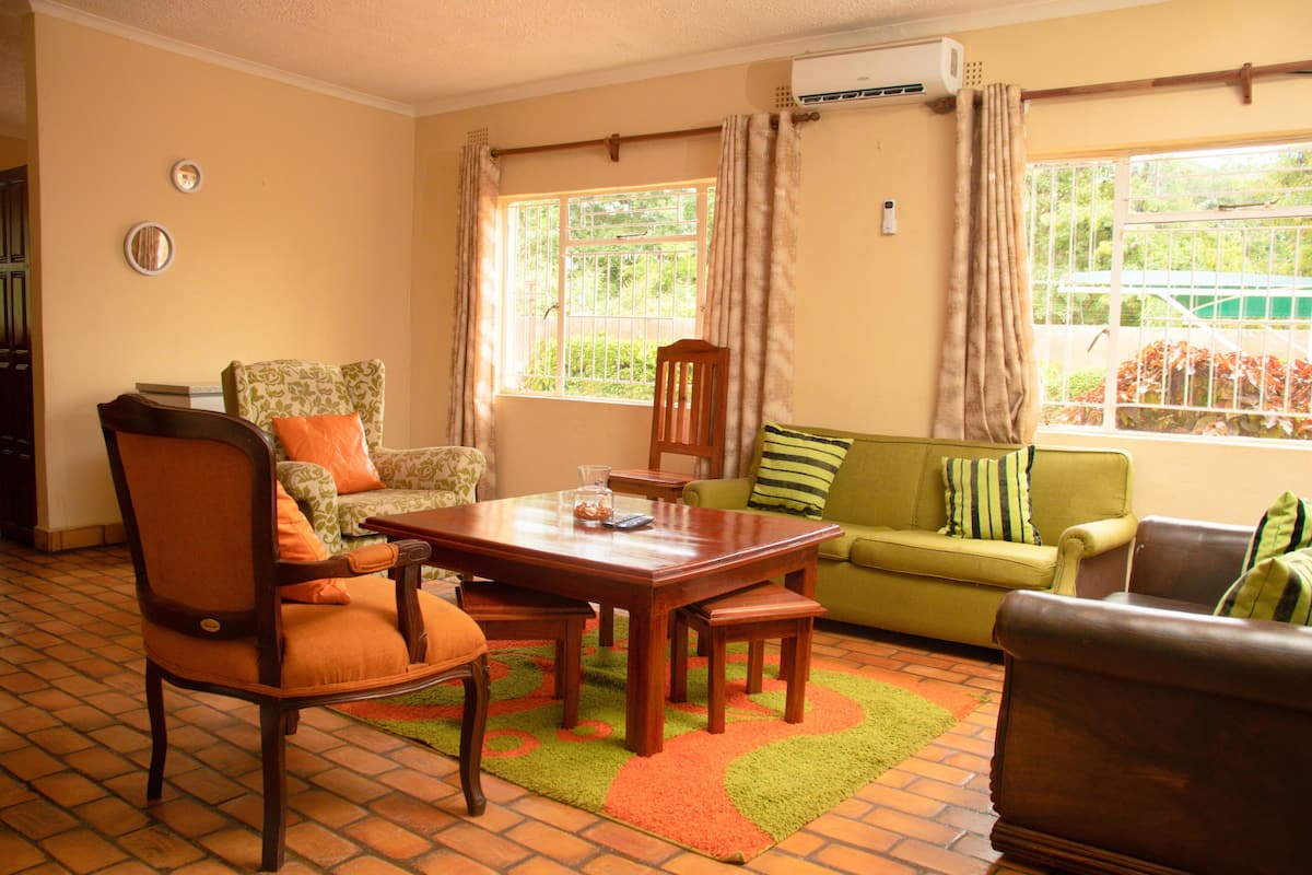 A living room with a wooden dining table, two chairs, a sofa, and a green armchair.