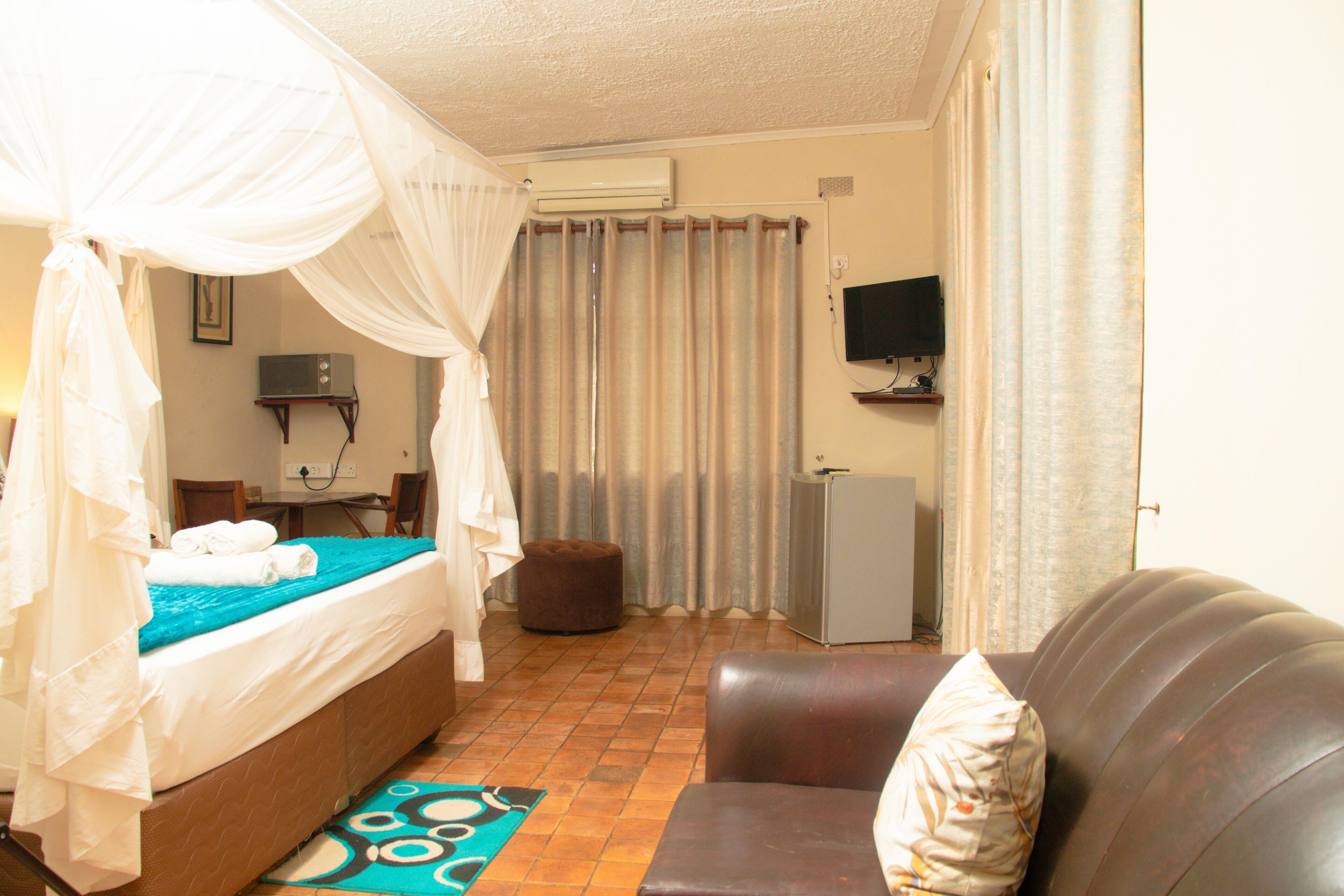A bedroom with a bed, a television, a refrigerator, and a couch.